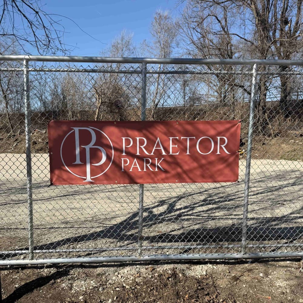 The red Praetor Park banner zip-tied to the chain-link fence at Lot B